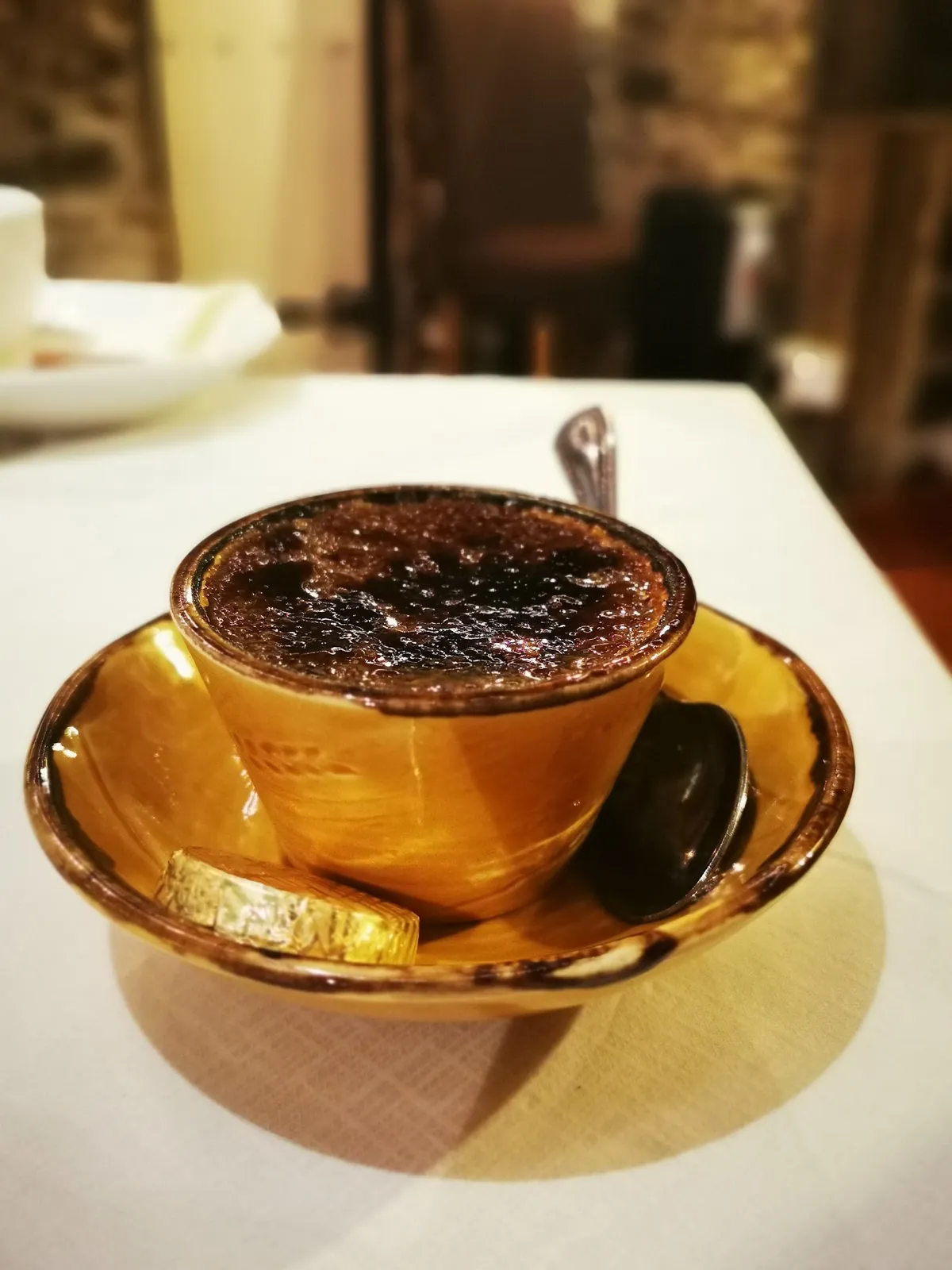 Cr&egrave;me br&ucirc;l&eacute;e in an amber ceramic cup, softly lit in the dim dining room